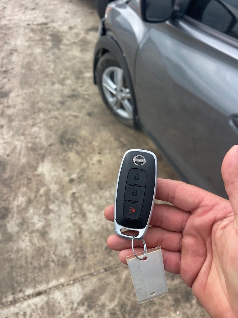 Technician holding a programmed Nissan smart key fob with vehicle in background